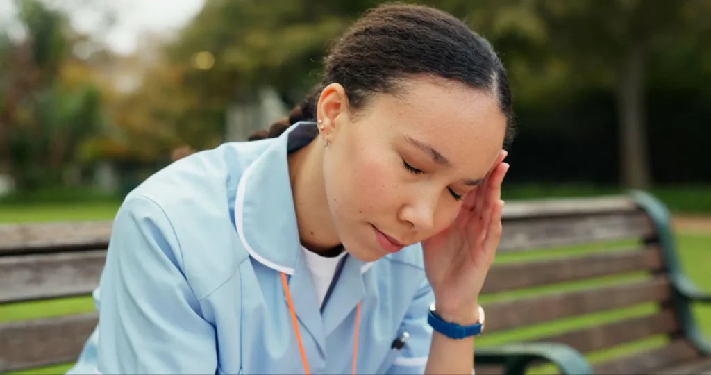 A tired nurse sitting on a hospital bench with her head in her hands after a long shift.