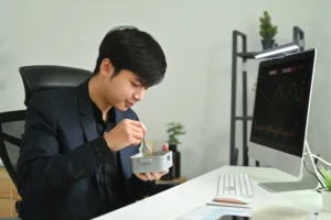 A man sitting and eating in front of a desktop.