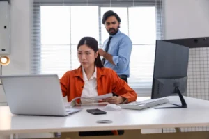 A man is standing behind a woman sitting at a desk.