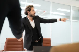 A man in an office, angrily pointing in a direction with his hand.